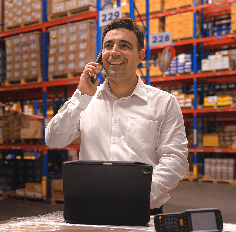 Man in a warehouse using a phone and a laptop