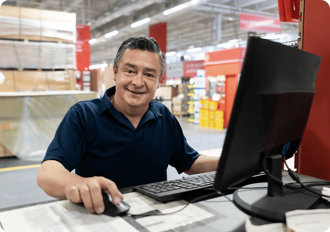 Image: A man sitting at a computer in a warehouse.