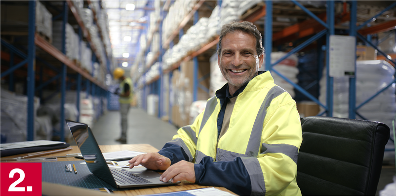 Image: A man sitting at a computer in a warehouse.