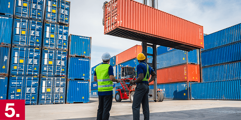 Image: Two men watching a shipping container being unloaded.